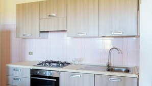 Uma cozinha com armários de madeira clara, fogão de aço inoxidável, pia e painel de azulejos.