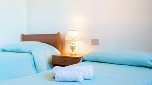 Uma cama com cabeceira de madeira, um criado-mudo com abajur e duas almofadas.