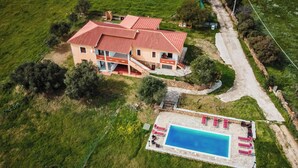 Vista aérea de uma casa com piscina, cercada por vegetação.
