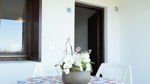Uma área de jantar com uma mesa posta para dois, um vaso de flores brancas e uma janela com vista.