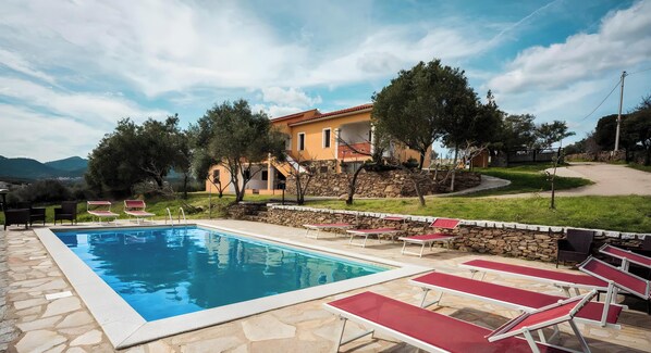 Une piscine avec des chaises longues, un mur en pierre et un bâtiment avec un toit rouge.