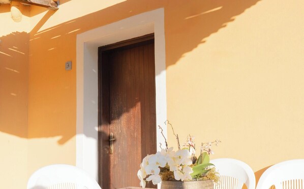 A door with a number '3' above it, a dark wooden door, and a white chair with a potted orchid plant beside it.