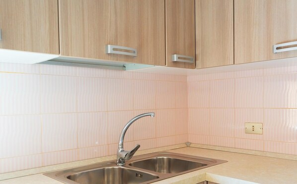 Una cocina con dos lavamanos de acero inoxidable, armarios de madera y paredes cubiertas de baldosas rosa claro.