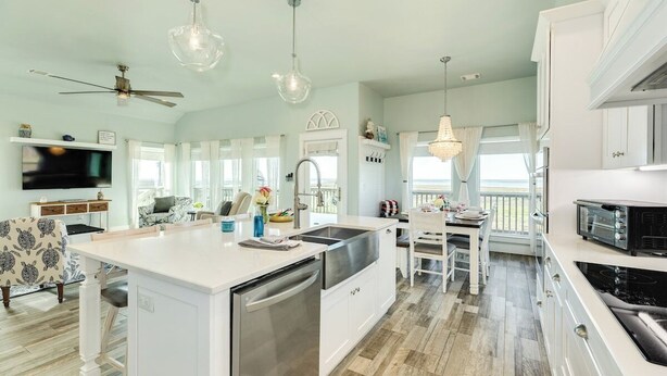 A spacious kitchen with a central island, white cabinetry, and a dining area with a view. - Sunchaser (Galveston)