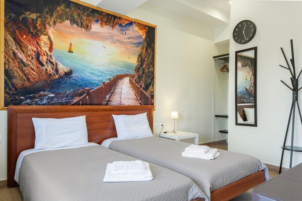 A hotel room with two beds, a painting of a coastal scene, a clock, and a mirror.
