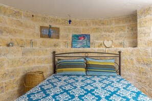 Ein Schlafzimmer mit Stehwänden, einem Bett mit gemusterten Textilien, einem Korbwesen und einem Gemälde.