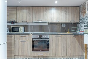 Eine moderne Küche mit Holzausstattung, einer Mikrowelle, einem Backofen und einer kleinen Kochinsel mit Wasserkocher.