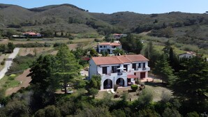 A two-story house with a red-tiled roof, surrounded by lush greenery and hills.