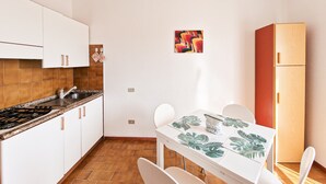 A compact kitchen with a stove, sink, and white cabinets. There's a dining table with chairs and a small refrigerator.
