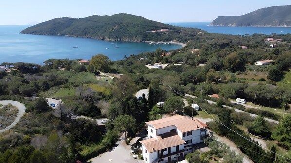 A coastal property with a white building, a road, and a view of the sea and hills.