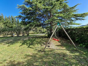 Eine Schaukel auf einer grünen Wiese mit Bäumen und blauem Himmel.