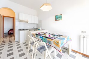 Eine moderne Küche mit weißen Schränken, ein Essbereich mit bunten Tischdecken und einem gemusterten Boden.