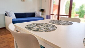 Una mesa de comedor con dos individuales, un sofá azul y una ventana que da a zonas verdes.