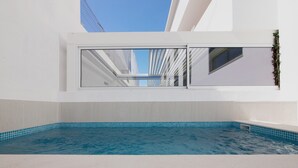 Een modern binnenzwembad met helderblauw water, witte wanden en een dakraam erboven.