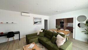 Een moderne woonkamer met een groene bank, een houten salontafel, en een eethoek met een houten tafel.
