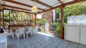 A covered patio with stone flooring, white plastic chairs, a wooden table, and hanging pendant lights. - Apartment 'Casa 20' with Private Terrace, Wi-Fi and Air Conditioning (Stintino)