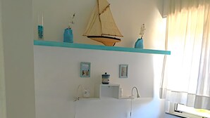 A bedroom with a bed, a nightstand, a shelf with decorative items, a window with curtains, and a wall-mounted shelf with a small plant.