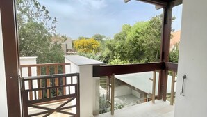 A balcony with a wooden railing, a view of trees and buildings, and a tiled floor.