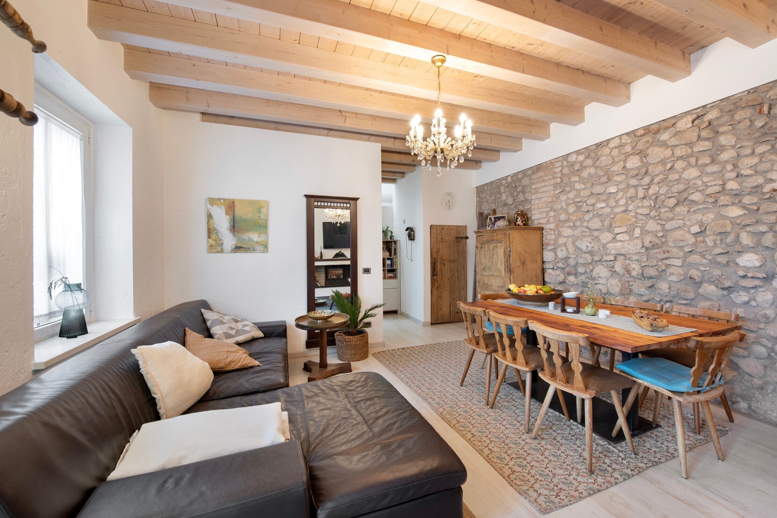 Ein Wohnzimmer mit einer Couch, einem Esstisch mit Stühlen, einer Kandelaber und einer Steinwand.
