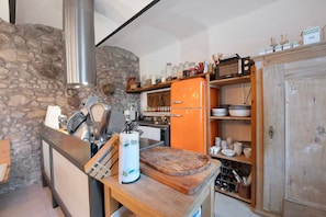 Cocina con pared de piedra, encimera de madera, estufa moderna y refrigerador naranja vintage.