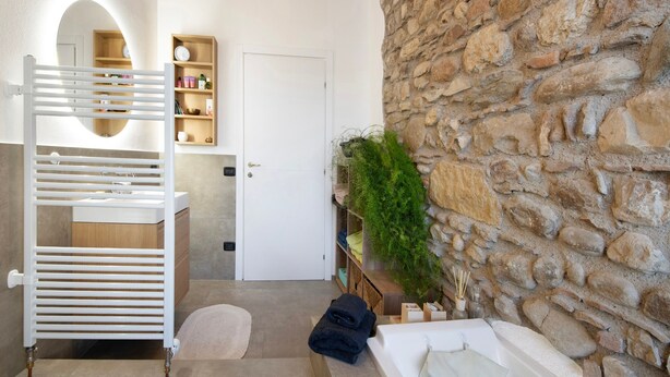 A bathroom with a white bathtub, a towel rack, a shelf with toiletries, and a stone wall. - Holiday Home 'Haus Siloah Grole Di Desenzano' with Private Garden and Wi-Fi (GROLE di Desenzano)