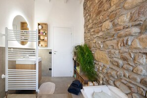 Un baño con una bañera blanca, un perchero para toallas, un estante con artículos de aseo y una pared de piedra.