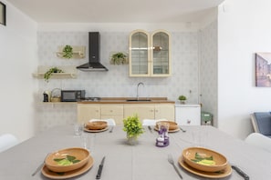 Cozinha moderna com armários brancos, coifa preta e área de refeições com mesa posta para quatro pessoas.