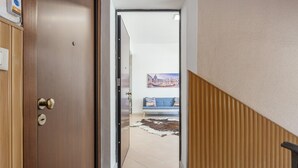 Een hal die leidt naar een kamer met een blauwe bank, een houten vloer en een deur met een messing handgreep.