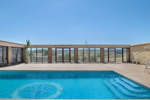 En swimmingpool med fri utsikt över det omgivande landskapet, en pergola med ett tak av tegelpannor och en stenmur.