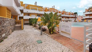 A courtyard with a swimming pool, a stone wall, and a sign indicating pool hours. - Apartment 'Royal Cabanas Golf' with Shared Pool, Wi-Fi and Air Conditioning (Conceição de Tavira)