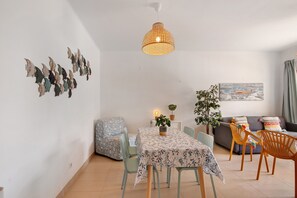 Een eetgedeelte met een tafel, stoelen, een hanglamp, een bank en een muur met kunstwerken.
