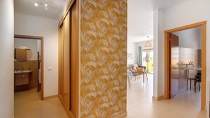 A hallway with a patterned wall, a kitchen area with a refrigerator, and a dining area with chairs and a table. - Apartment 'Royal Cabanas Golf' with Shared Pool, Wi-Fi and Air Conditioning (Conceição de Tavira)