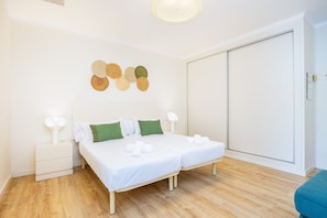 A bedroom with two beds, a nightstand, a wall-mounted lamp, and a wardrobe.