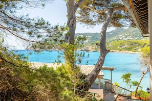 A coastal view with a staircase leading to a covered area, surrounded by trees and overlooking a clear blue sea.