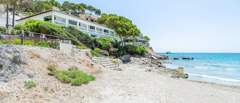 Una propiedad costera con playa, una escalera que lleva a una casa y vista al mar.