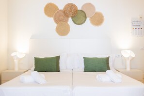 Una habitación de hotel con dos camas, almohadas verdes, una obra de arte en la pared y un reloj de pared iluminado.