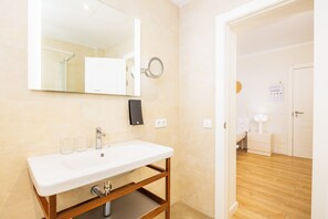 Un baño con lavamanos blanco, espejo y tocador de madera.