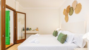 Een slaapkamer met een bed, kussens, een nachtkastje en een kunstwerk aan de muur.