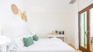 Un lit bien fait, avec des oreillers, une table de chevet avec une lampe, et une vue sur l’extérieur grâce à une porte vitrée.