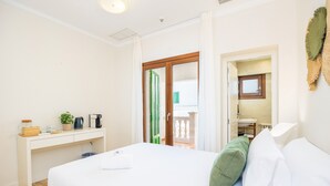 Une chambre avec un lit, un bureau, une machine à café, une plante et une vue sur un balcon.