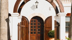 A white building with a wooden archway, a large wooden door, and a potted plant. - Hostal Boutique Canyamel 110 Single Room with Partial Sea View, Terrace, Wi-Fi and A/C (Canyamel)