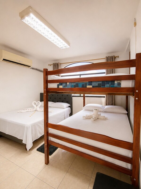 Habitación con literas, dos camas, ventilador de techo, equipo de aire acondicionado y ventana con cortinas.