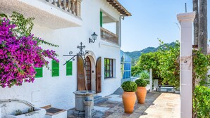 A white building with green shutters, a stone well, and potted plants. - Hostal Boutique Canyamel, 112 Double Room with Sea View, Private Terrace, Wi-Fi and Air Conditioning (Canyamel)