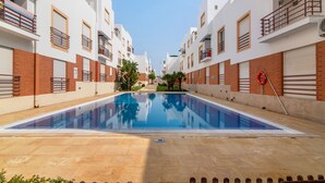 Una piscina rodeada de edificios de varios pisos con balcones y un cielo despejado.