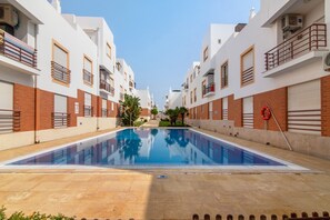 A swimming pool surrounded by multi-story buildings with balconies and a clear sky. - Duplex Apartment in Cabanas de Tavira with Shared Pool, Wi-Fi, and Air Conditioning (Tavira)
