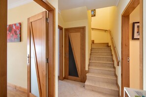 Un couloir avec des portes en bois, un escalier et un petit tableau encadré accroché au mur.