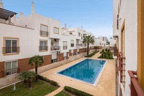 A residential building with a swimming pool, balconies, and a clear sky.