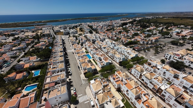 Vista aérea de una zona residencial costera con viviendas ordenadas, una avenida central y una playa al fondo.