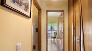 Un pasillo con un cuadro en la pared, un interruptor de luz y una silla al fondo.