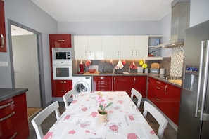 Een moderne keuken met rode kastjes, een witte eettafel en een centraal keukenblok met een bloemenvaas.